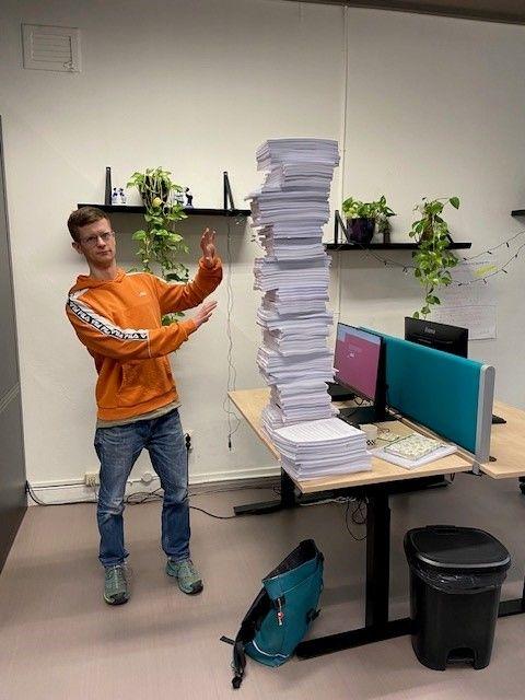 Op de foto liggen op een tafel de 113 dagvaardingen opgestapeld. Naast deze stapel staat een werknemer van !WOON.